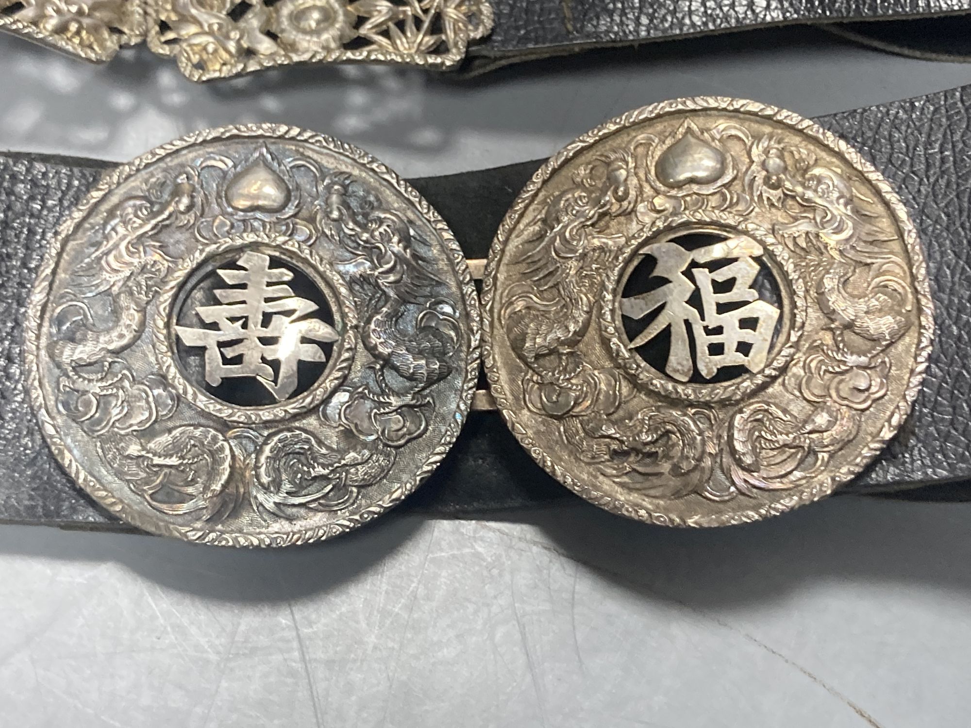 A Chinese white metal cigarette case by Luen Hing, 75mm and four pairs of Chinese white metal belt buckles, three mounted on leather